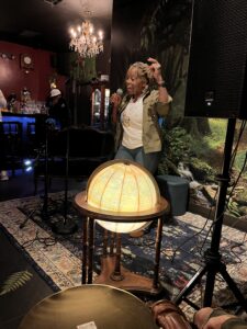 Open mic at The Wicked Wolf. A woman is reciting in front of a microphone. There's a lit world globe in the foreground.