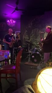 Dueling saxophones playing jazz at The Wicked Wolf, underneath a chandelier with purple lighting.