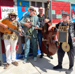 Robby Ravenwood and the Funhouse Porkupines band, carrying their instruments, in front of a colorful building.